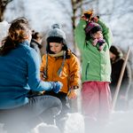 Eine Person sitzt in Hocke mit zwei Kindern im Kurpark Schierke und baut ein Iglo während der Schierker Wintersportwochen.